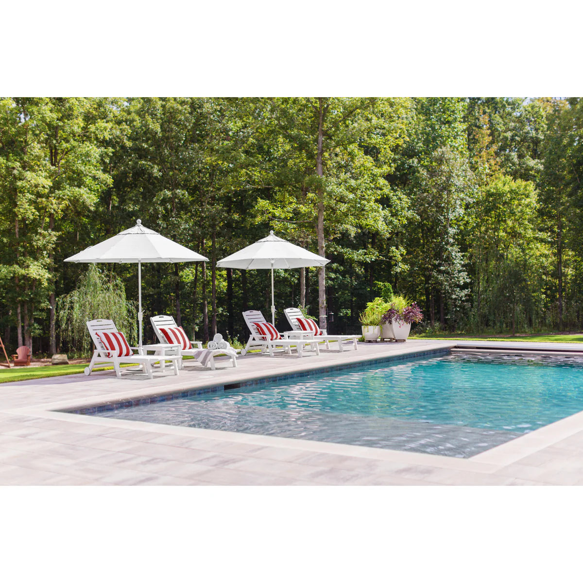 Pool area with lounge chairs and umbrellas surrounded by trees