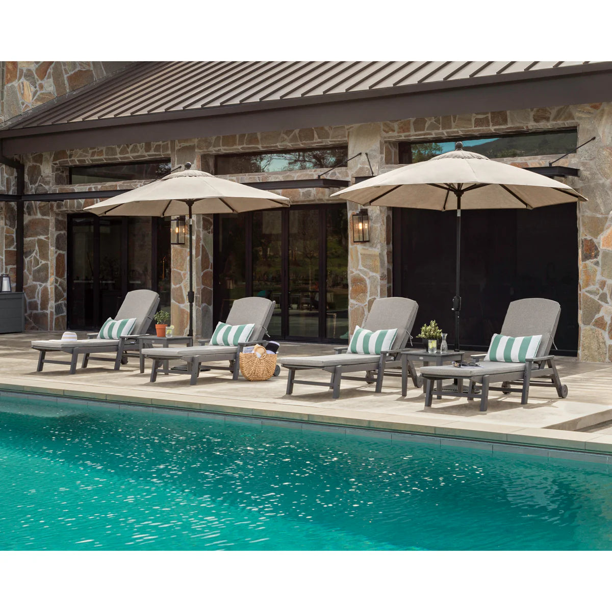 Outdoor patio set with lounge chairs, tables, and umbrellas by a poolside.