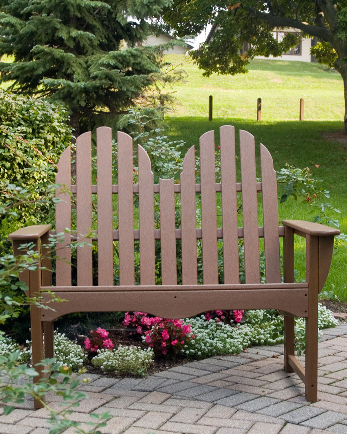 POLYWOOD Classic Adirondack 48" Bench in Teak in a garden surrounded by pink flowers