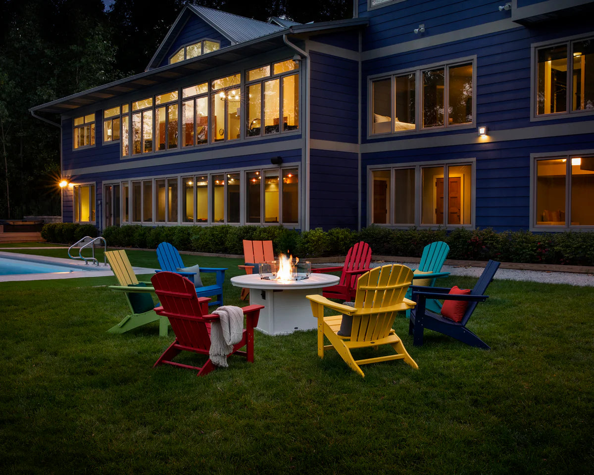 Colorful outdoor chairs around a fire pit in front of a large blue house at night.