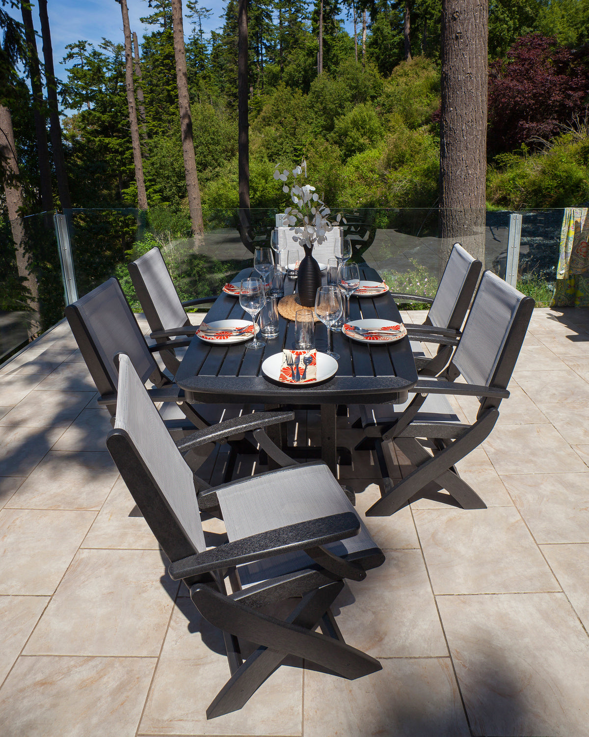 Black POLYWOOD Coastal Folding Chairs with gray slings at a set dining table on a wooded lakeside patio