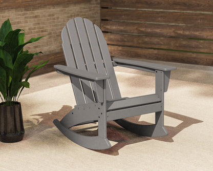 Slate Grey POLYWOOD Vineyard Adirondack Rocking Chair on a sunny patio beside a potted plant and wood-slat wall