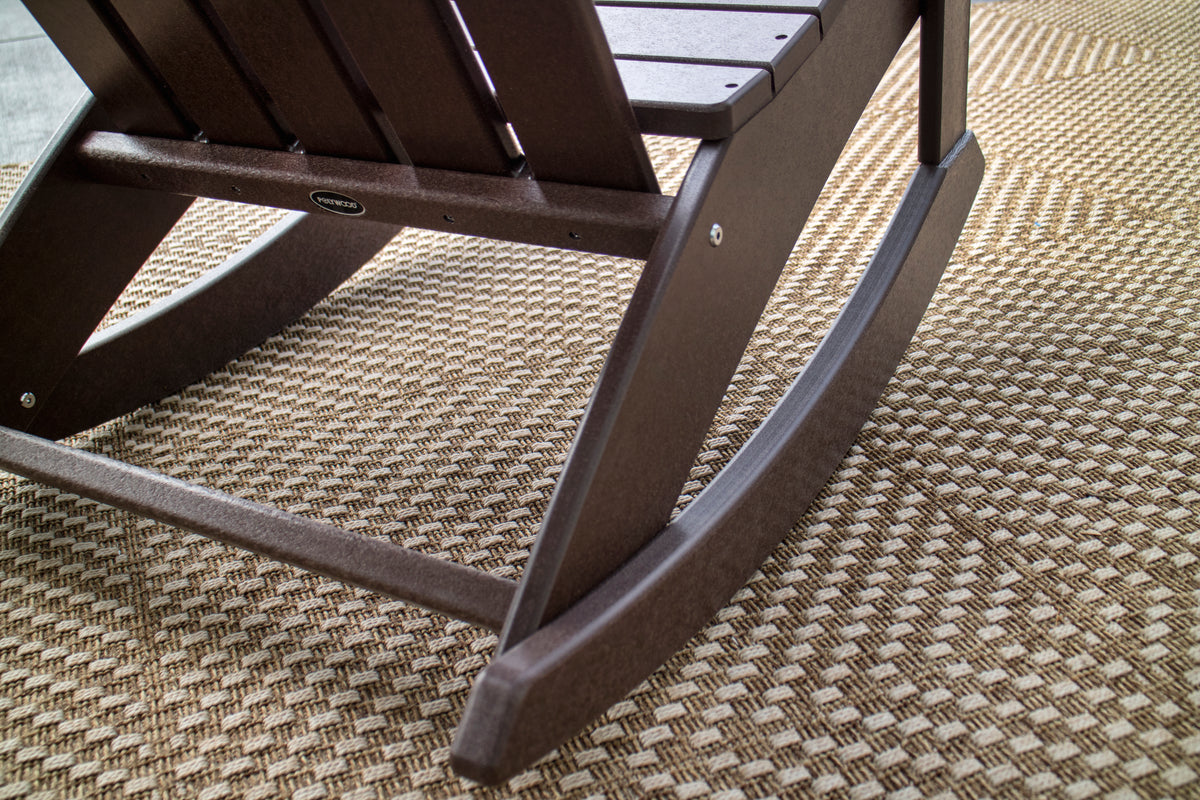 Close-up of the rocker runner and arm of a Mahogany POLYWOOD Adirondack rocking chair on a woven rug
