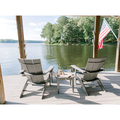 Two Adirondack chairs on a deck overlooking a lake with an American flag in the background.