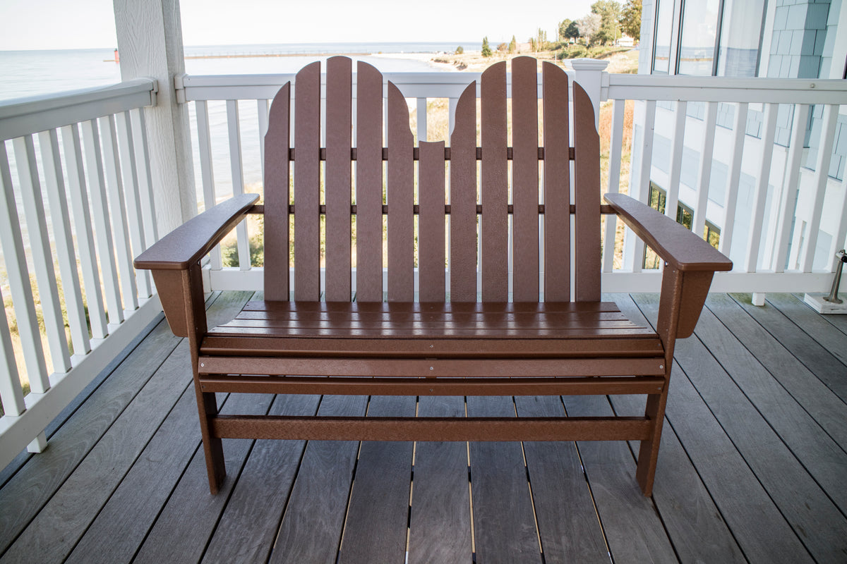 Front view of the POLYWOOD Vineyard 48" Adirondack Bench in Teak on a seaside porch with white railings