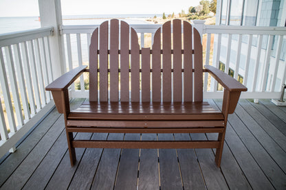 Front view of the POLYWOOD Vineyard 48" Adirondack Bench in Teak on a seaside porch with white railings