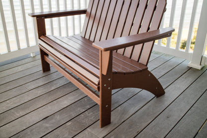Angled view of the POLYWOOD Vineyard 48" Adirondack Bench in Teak with wide arms on a wood deck