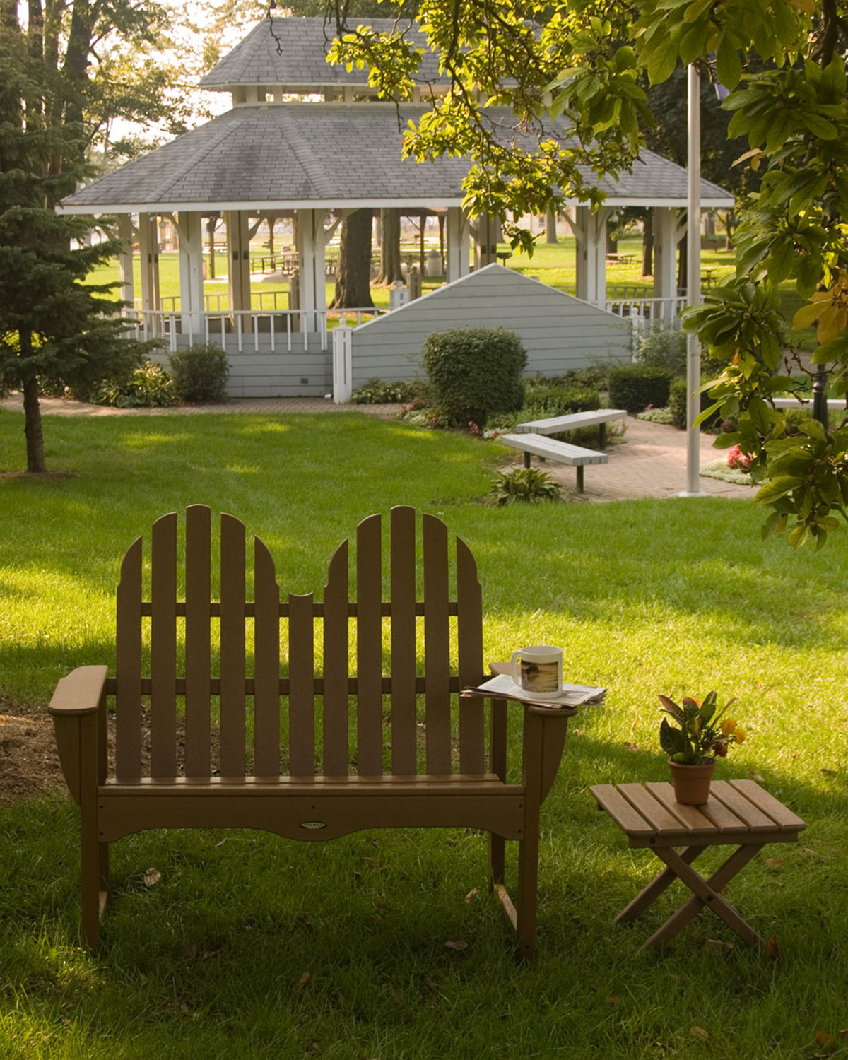 Teak POLYWOOD Classic Adirondack 48" Bench on a lawn next to a matching side table and gazebo