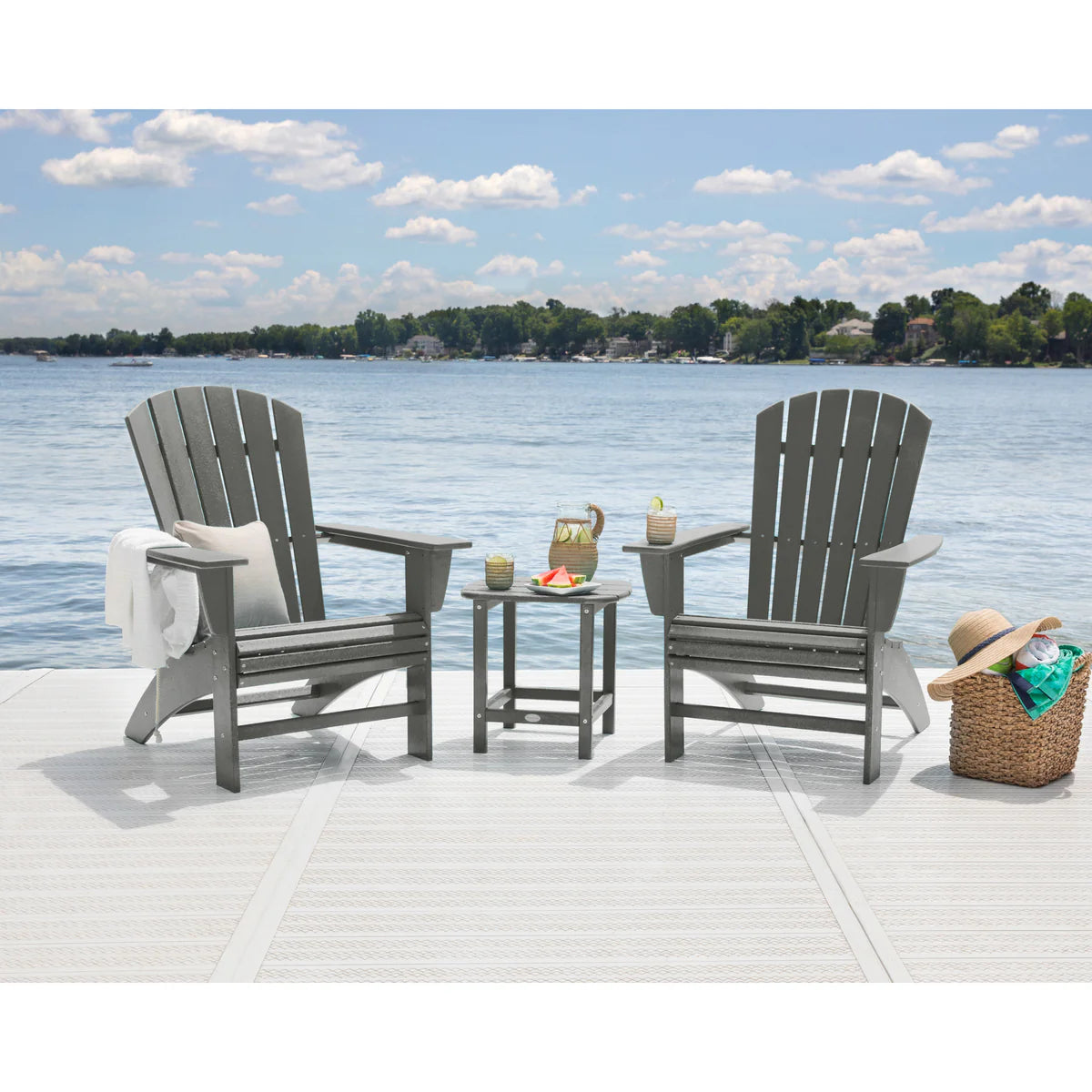 Two gray Adirondack chairs with a small table on a dock by a lake.