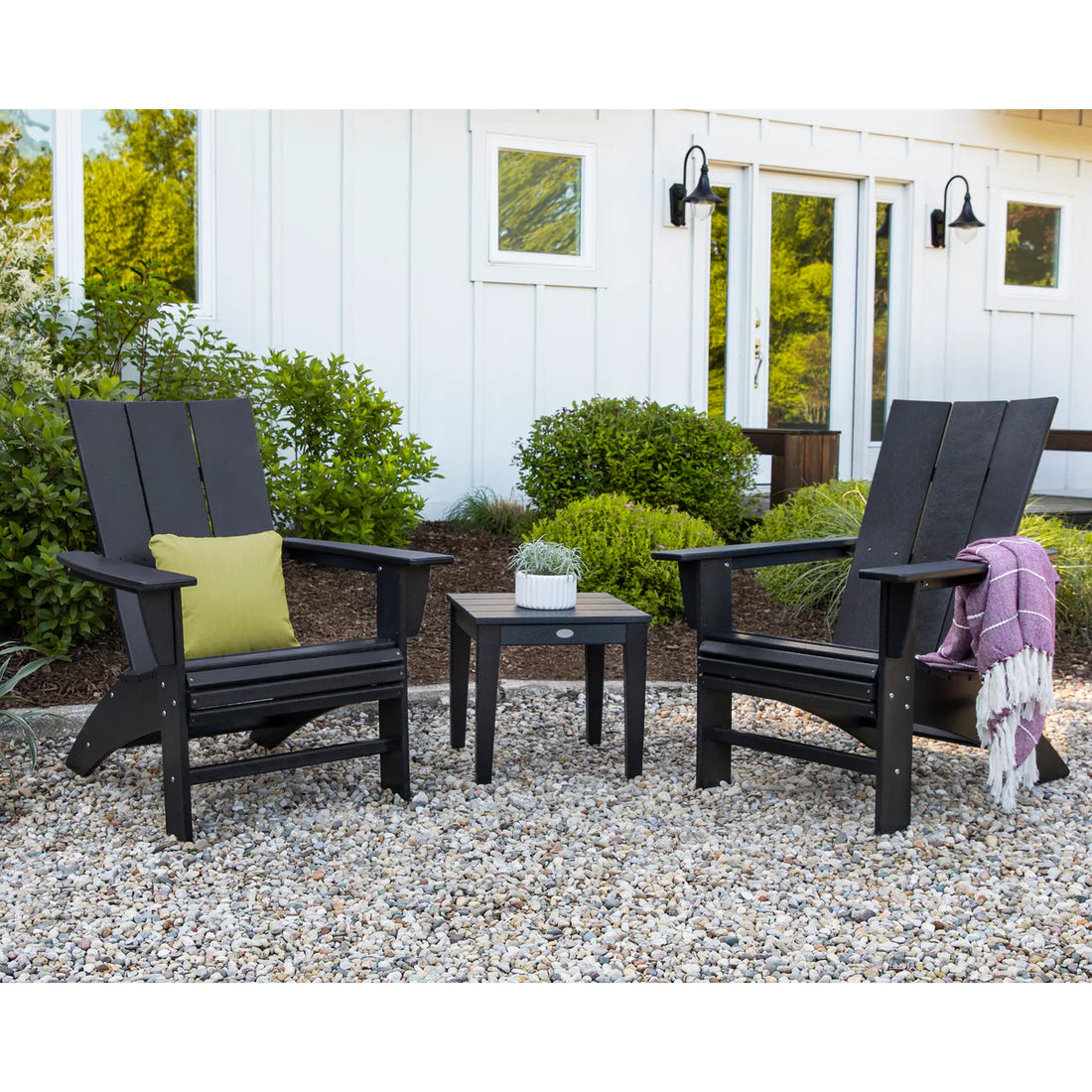 Two black Adirondack chairs with a small table in a garden setting.