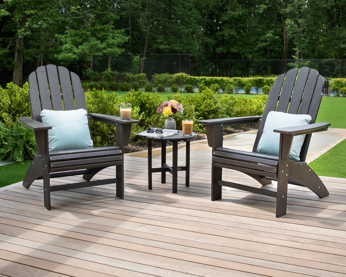 Two Adirondack chairs with cushions on a wooden deck with a small table.