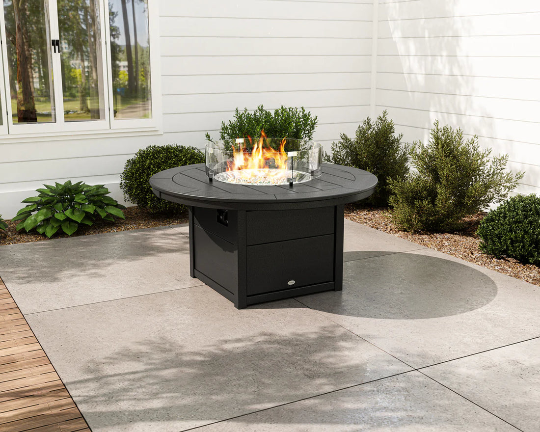 Black fire pit table with flames on a patio area with plants and a building in the background