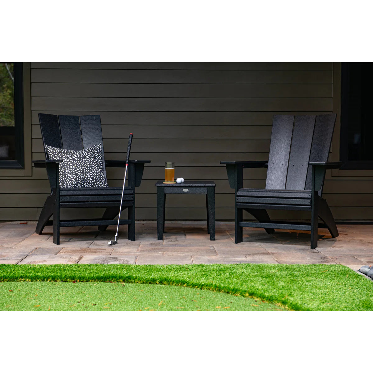 Two black Adirondack chairs with a small table on a patio.