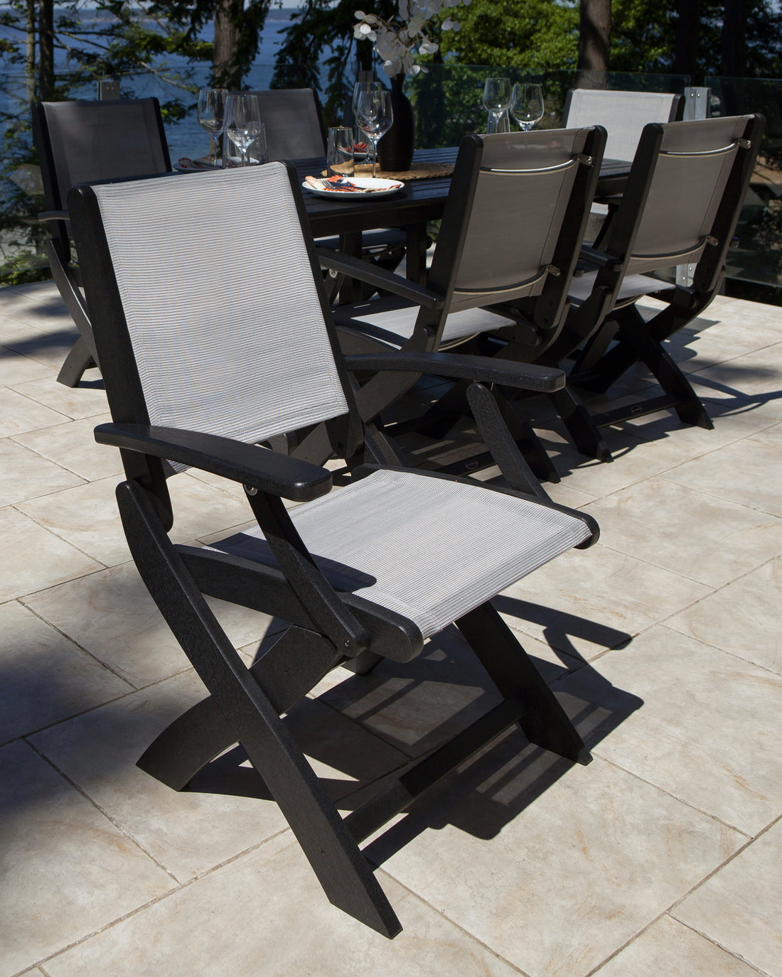Black POLYWOOD Coastal Folding Chairs with gray sling seats around an outdoor dining table on a stone patio