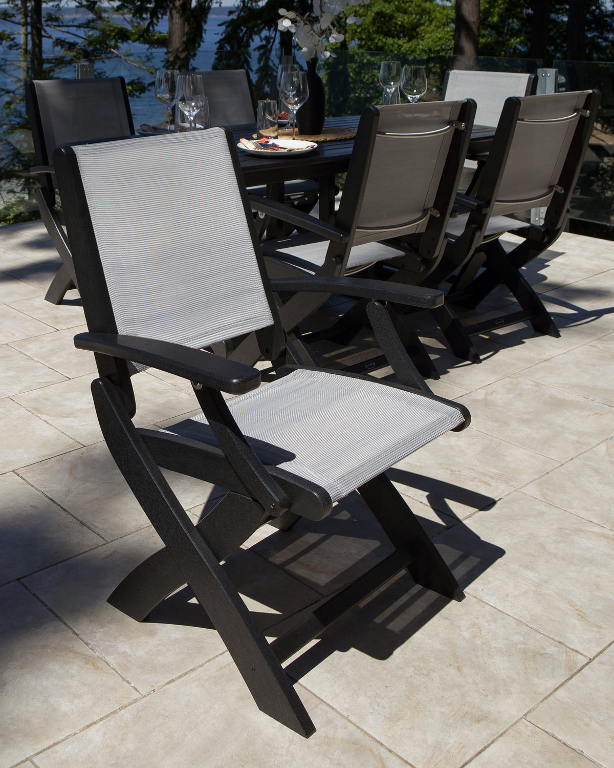 Black POLYWOOD Coastal Folding Chairs with gray sling seats around an outdoor dining table on a stone patio